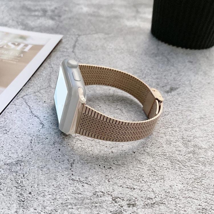 Buckle style steel replacement watchband for Apple Watch sitting on a gray surface next to a coffee cup.